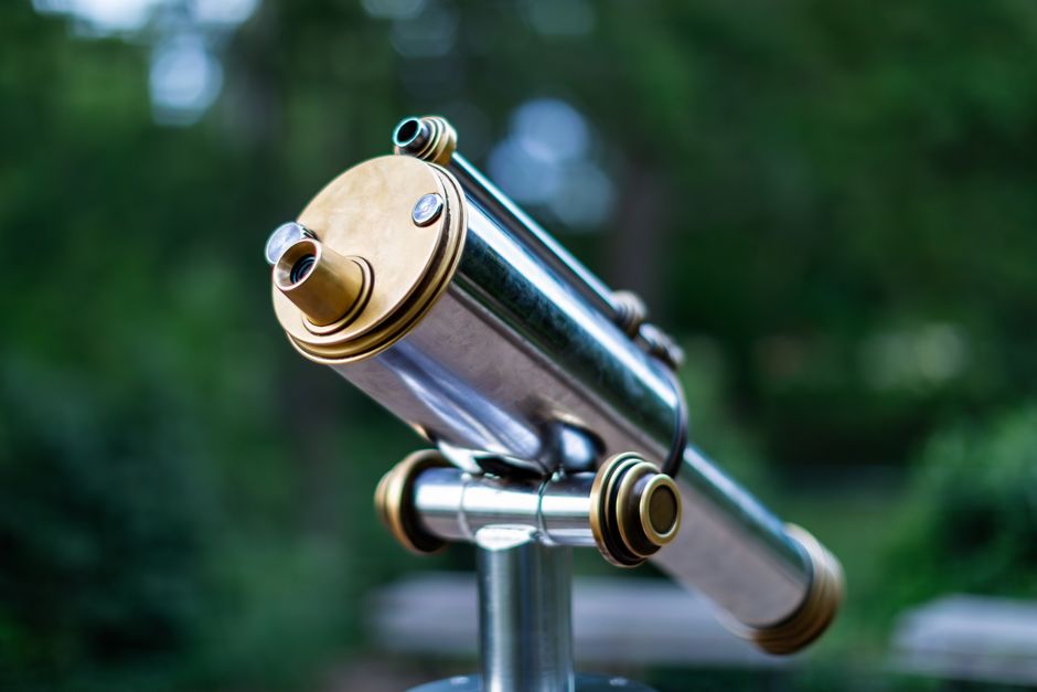 A classic outdoor telescope with a brass finish, set against a blurred natural background.